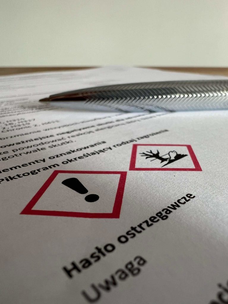 Zbliżenie na dokument z dwoma piktogramami ostrzegawczymi: wykrzyknikiem i martwym drzewem/rybą